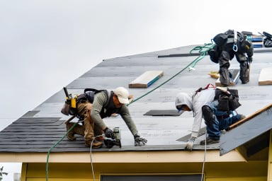 Two workers roofing a house with tools and equipment