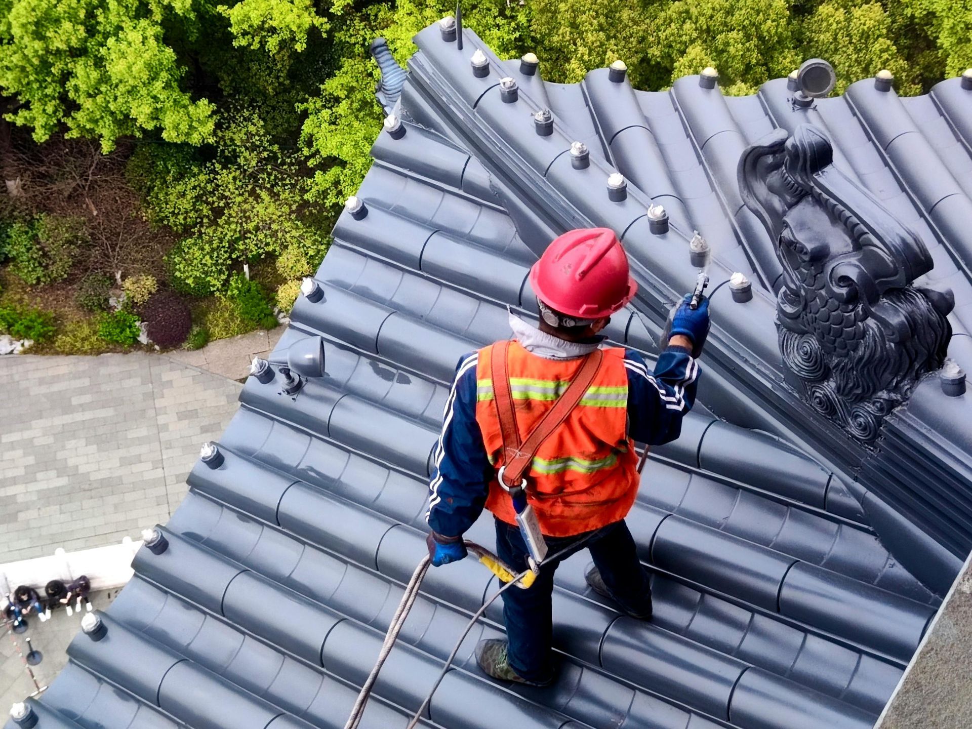 Worker in safety gear on a gray tiled roof.